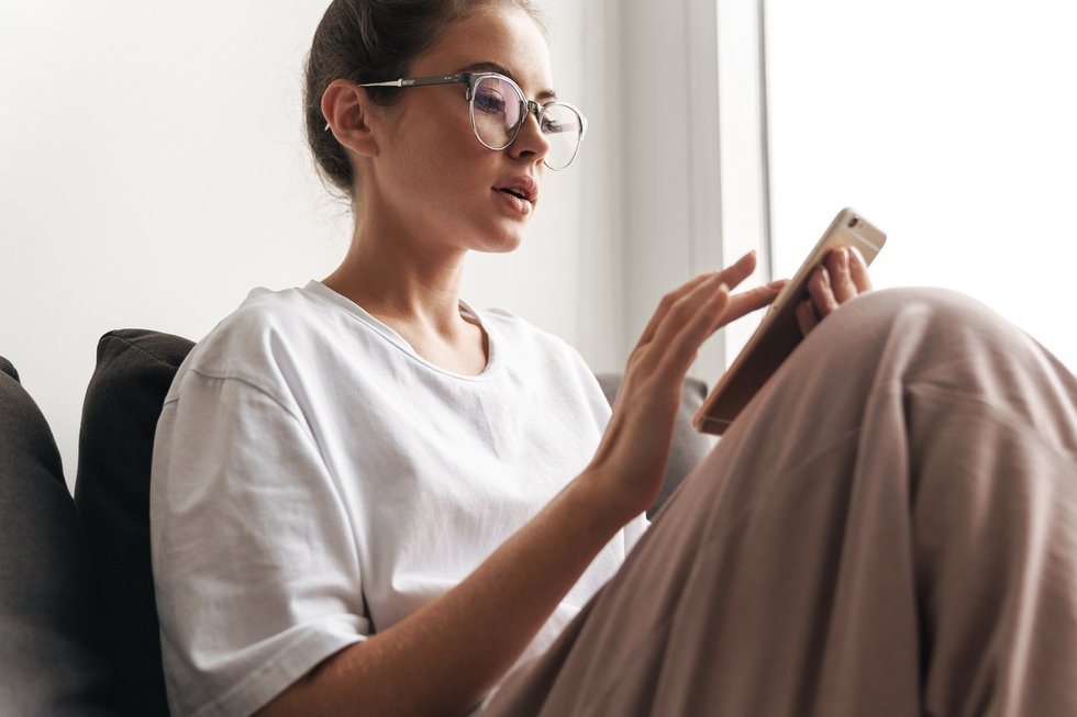 Image of focused woman typing on cellphone while sitting on sofa