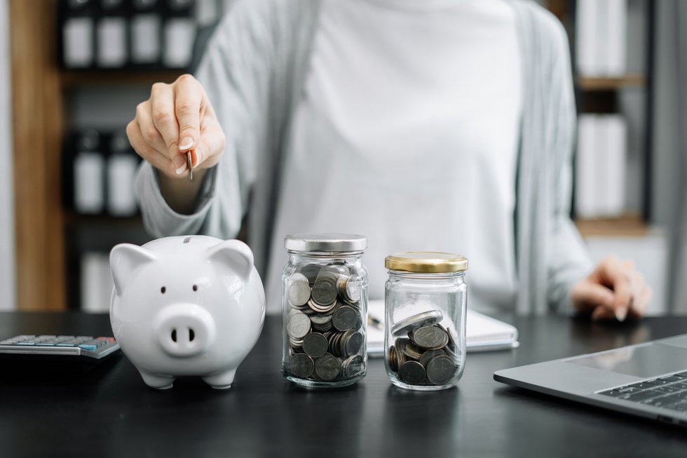 Woman sitting at desk managing expenses, calculating expenses, paying bills using laptop online, making household financial analysis, closer focus on the white piggy bank.